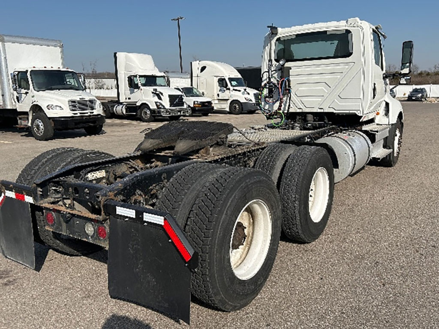 Truck tractor chassis and fifth-wheel area of a 2019 International LT625 from rear-left view with multiple white fleet trucks in background.