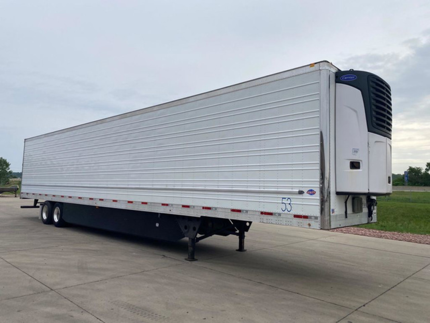 Trailer side view showing a refrigerated box truck trailer with a reefer unit at the front. Silver corrugated metal exterior, two axles, landing gear, and rear doors not visible.