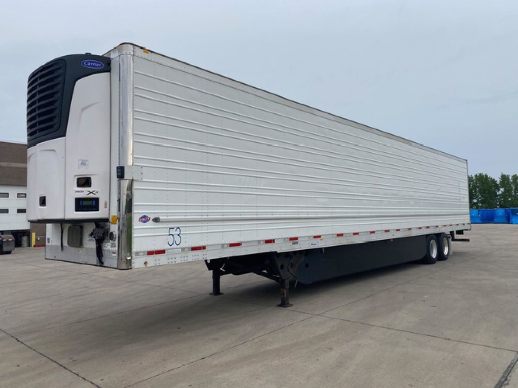 Trailer side view showing reefer unit at front of a white refrigerated semi-trailer with dual rear axles and landing gear. Visible text includes a blue Thermo King/Carrier unit at the front and small numbers on the side near the front corne