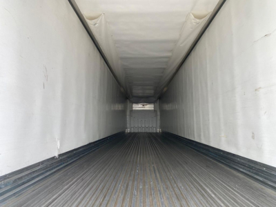 Trailer interior showing empty refrigerated trailer cargo area with ribbed floor and white interior walls, perspective toward the front door.