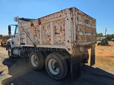 Dump truck showing weathered white cargo bed and dual rear axles with mud flaps.