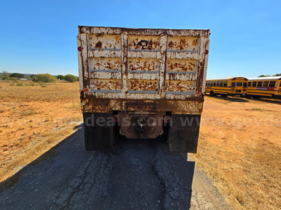 Dump truck rear showing rusted tailgate and bumper, with yellow school buses in background.