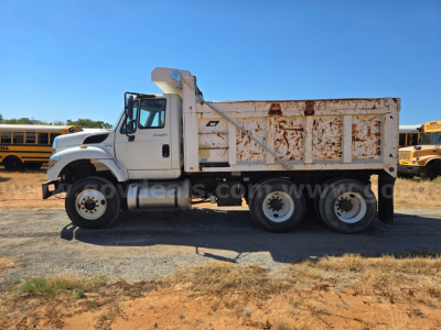 2013 International 7400 dump truck side view with white cab and rusted dumping bed.