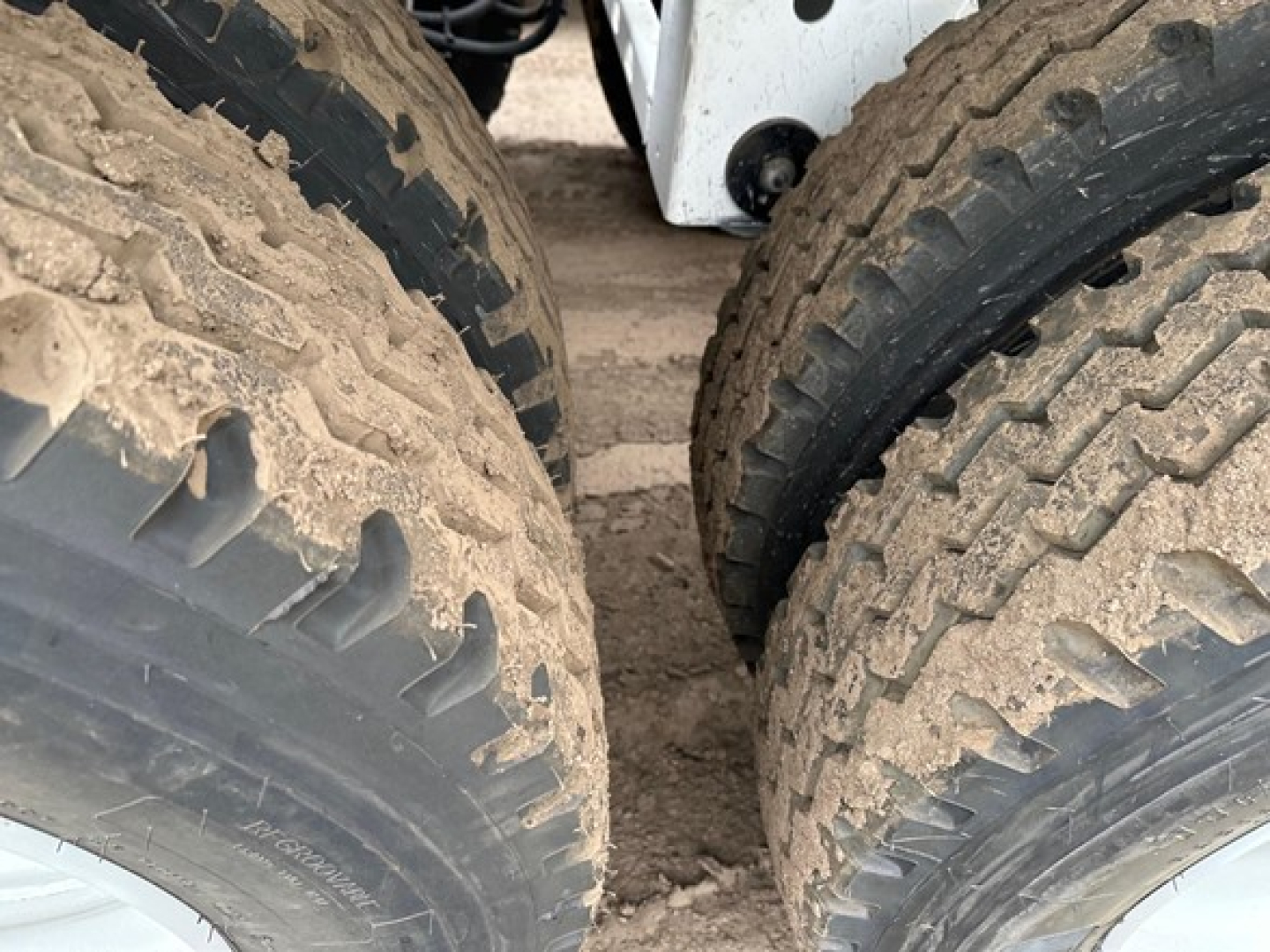 Bottom dump trailer tires and undercarriage visible, heavy tread, dirt on tires.