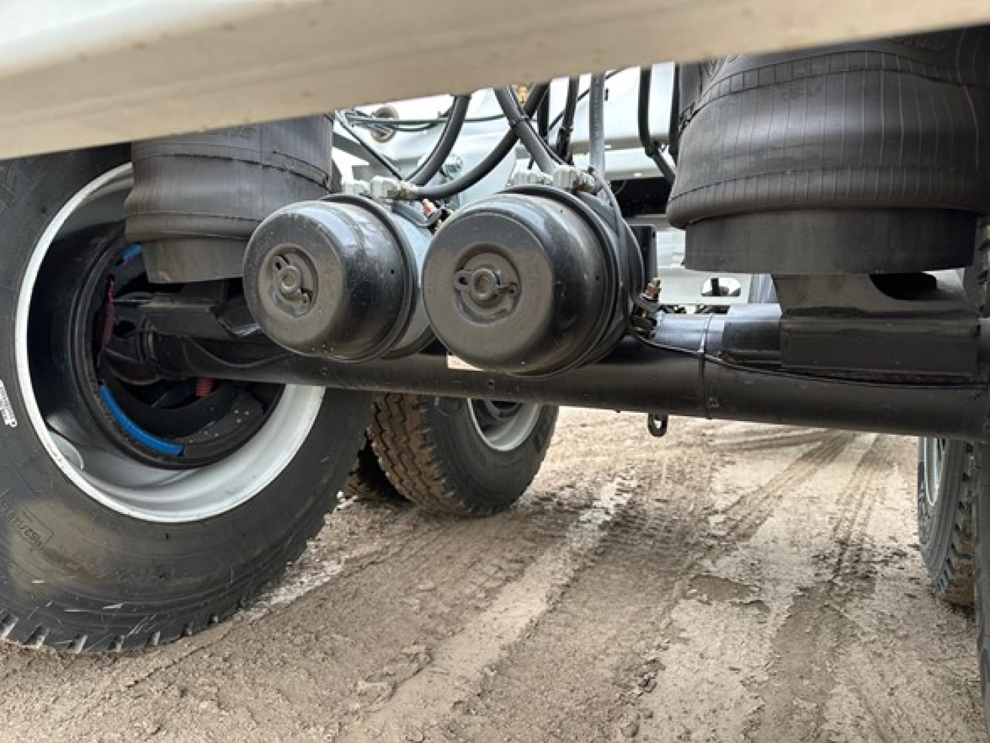 Bottom view of a new Dura Haul light weight bottom dump trailer showing dual air tanks and undercarriage piping between wheels.