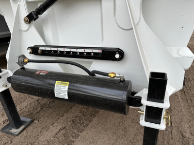 Trailer chassis showing hydraulic battery and level gauge with scale numbers from 0 to 10, and a black cylindrical component labeled with a warning sticker.