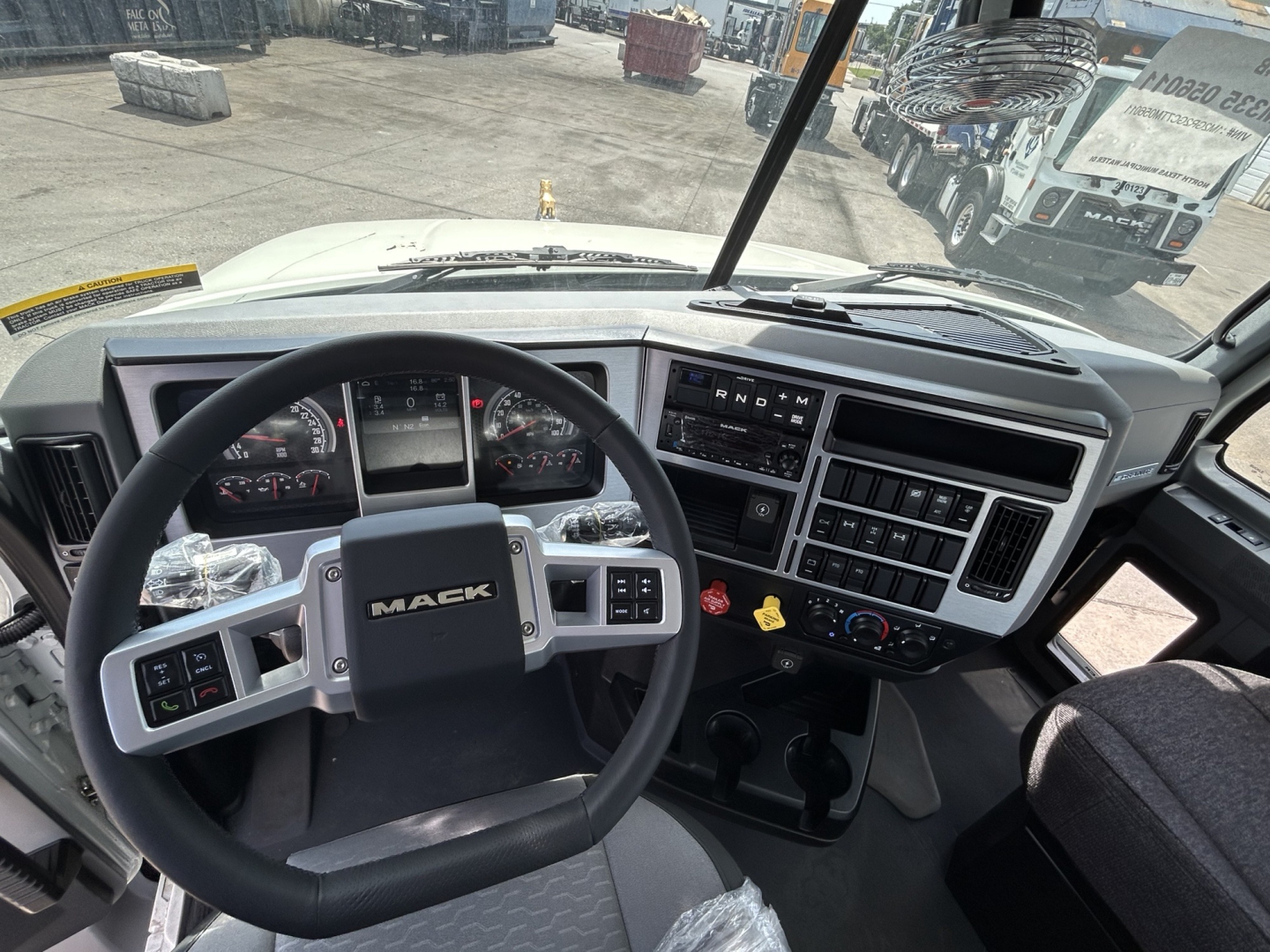 Rolloff truck cab interior showing Mack steering wheel, dashboard gauges, and control panel; windshield view of yard.