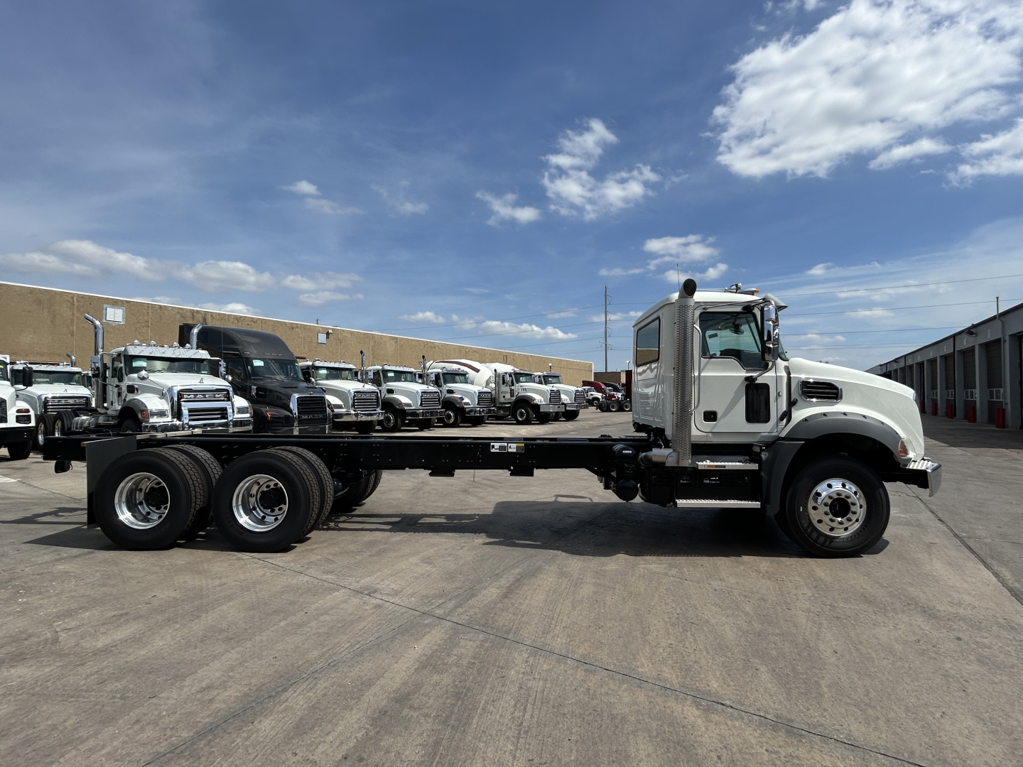 Mack GR64B roll-off truck in a parking lot showing chassis and cab with long wheelbase and empty frame rails.