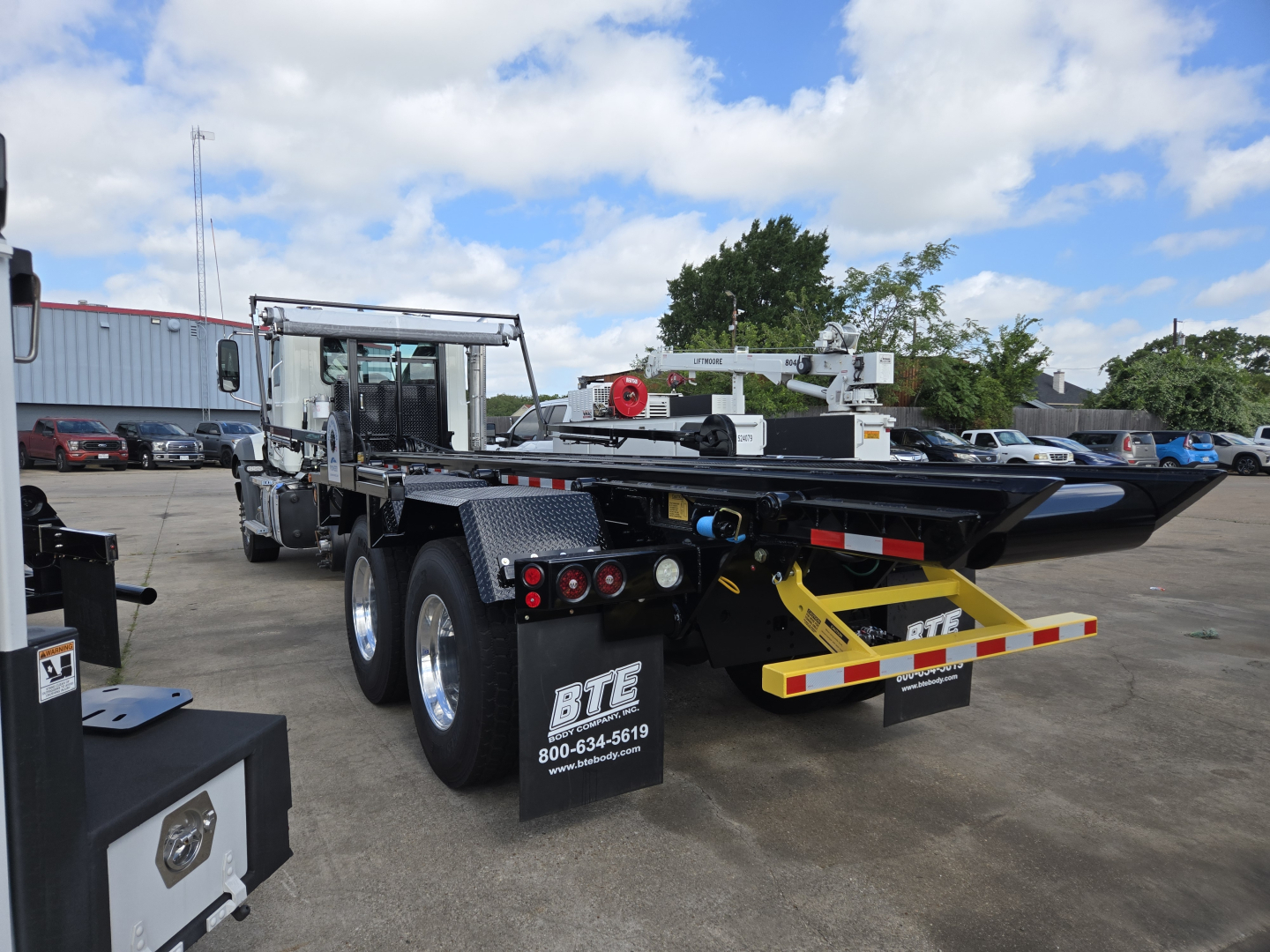 Mack GR64B roll-off truck trailer rear view with dual rear axles and metal deck, visible ladders, hydraulic components, and bumper; Rolloff category equipment.