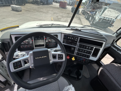 Rolloff truck cab interior showing Mack steering wheel, dashboard gauges, and control panel; windshield view of yard.