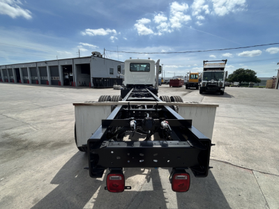 Chassis of a Mack GR64B roll-off truck showing rear frame, taillights, and fifth wheel area; clear blue sky and service bay in background.
