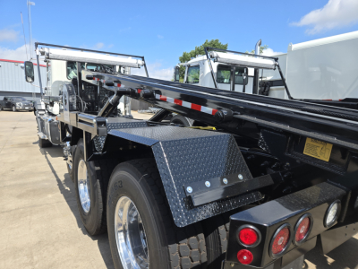 Mack GR64B roll-off truck chassis showing dual rear axles, diamond plate fenders, watermarked tool rack, and hydraulic boom mounts.