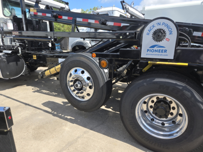 Truck chassis and wheels of a Mack GR64B rolloff with visible tires and a PioneerRack’n Pinion logo on the side.