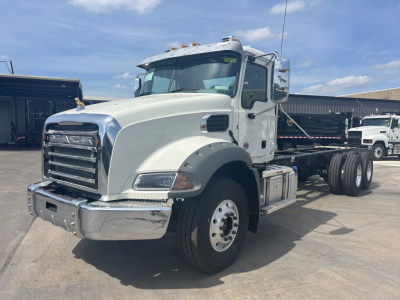 Mack GR64B roll-off truck shown in white cab with chrome bumper and dual rear axles, side exhaust, and large front grille.