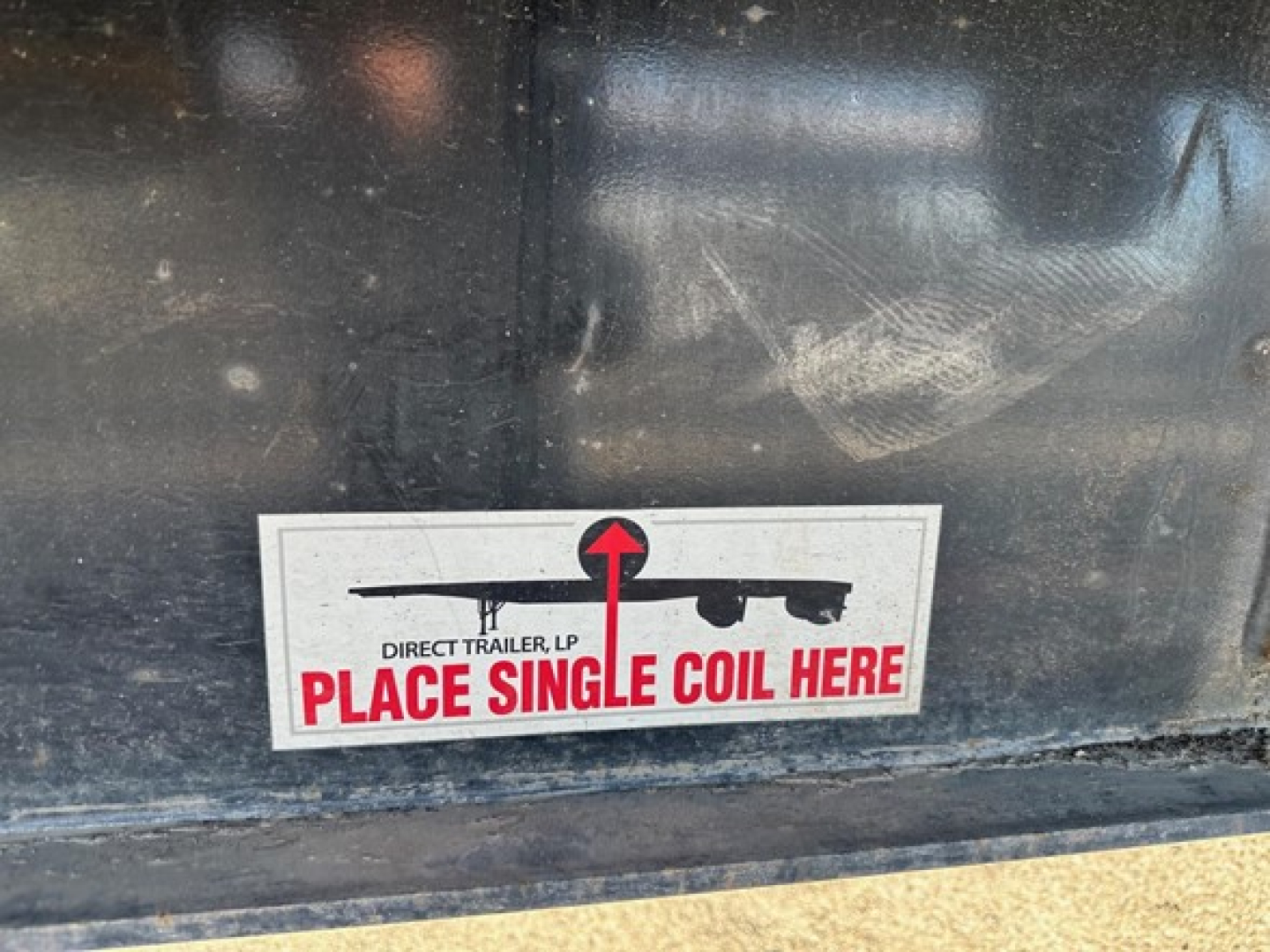 Sticker on black metal trailer indicating Direct Trailer, LP Place Single Coil Here with red and black graphic on white background.