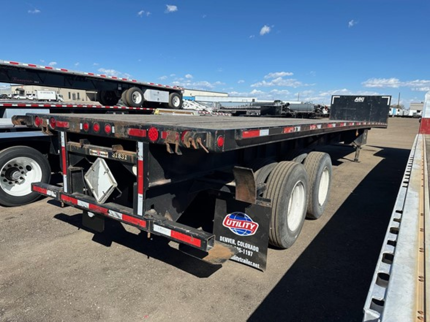 Flatbed trailer with dual rear axles and a pickup forklift kit, slight wear on deck, Utility brand mudflap and taillights visible