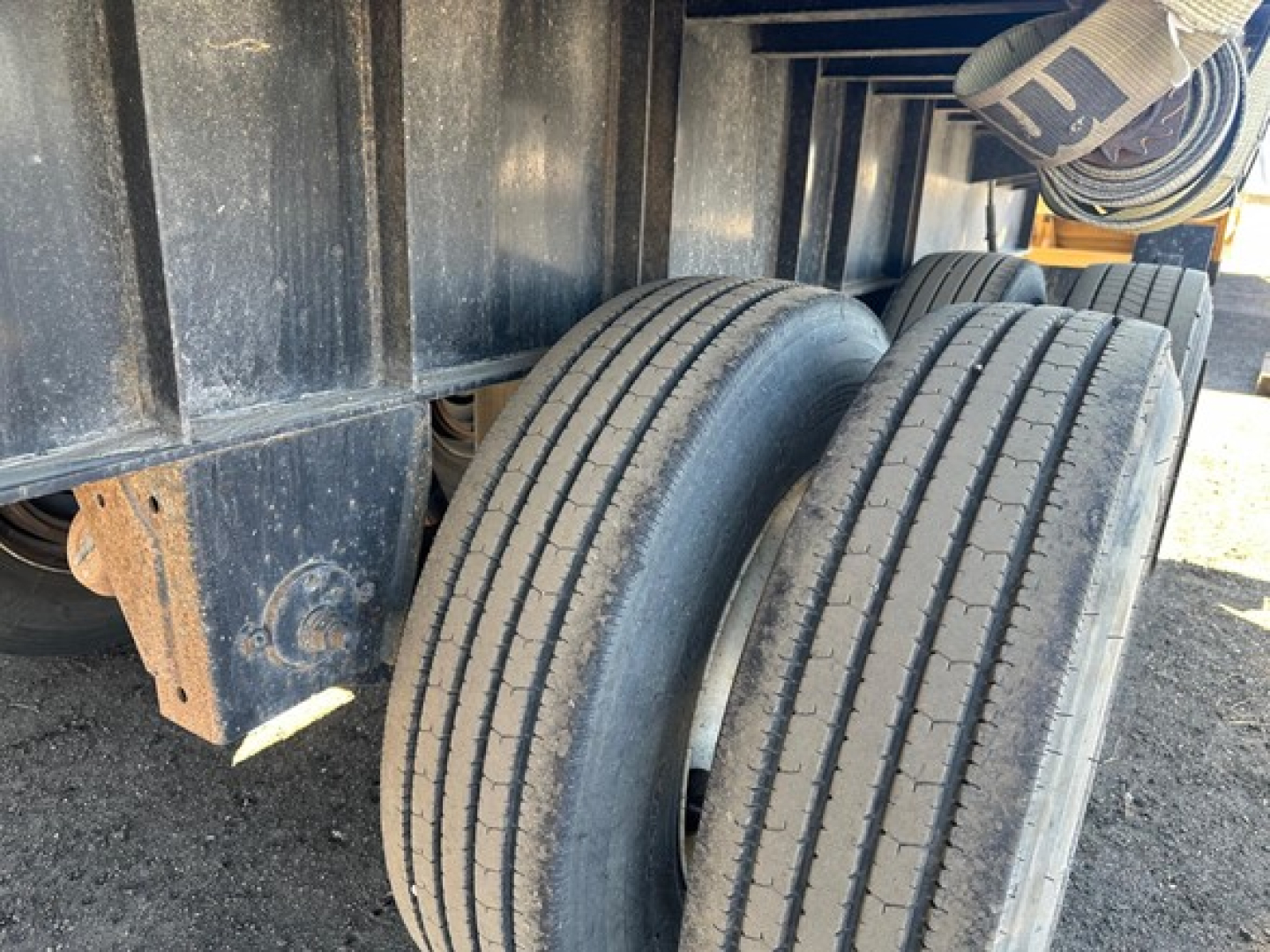 Trailer axle tires on flatbed trailer showing dual wheels and black metal frame, worn surface and road grime.