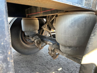 Direct air ride steel flatbed trailer undercarriage showing suspension air bags, axles, and leaf springs.
