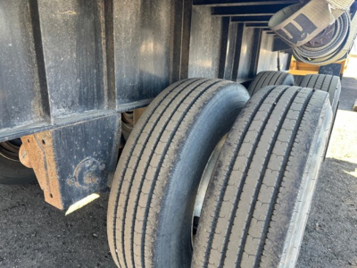 Trailer axle tires on flatbed trailer showing dual wheels and black metal frame, worn surface and road grime.