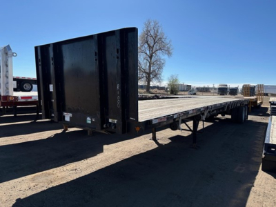 Flatbed trailer with forklift kit features in-service, low-angle view showing black steel bed and ramp on a trailer chassis.