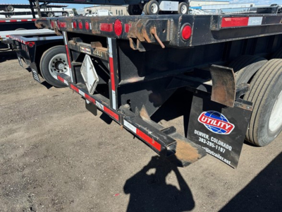Flatbed trailer rear view showing wheels, mudflap with Utility Industries logo, and reflective markers. Side rails and underside details visible.