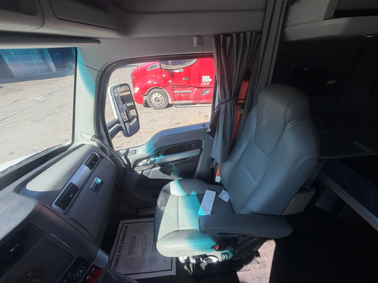 Kenworth T680 truck cabin interior showing driver's seat and dashboard with window, curtain, and side mirror.