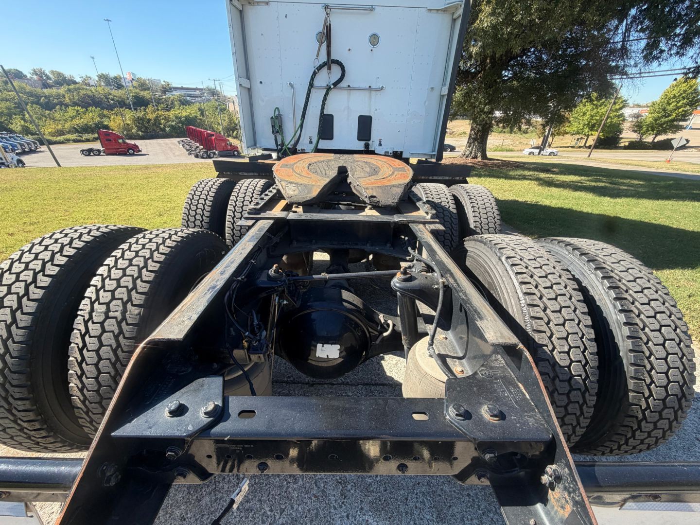 Rear view of a Kenworth truck chassis showing dual rear axles and fifth-wheel area. Visible components include framing rails, air lines, and drivetrain undercarriage.