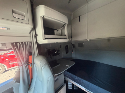 Kenworth T680 sleeper cab interior showing upper storage cabinet, fold-out bunk, and navigation console with seat in foreground.