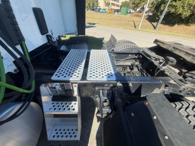 Kenworth T680 cab and chassis area showing metal perforated step/diamond plate steps and side components near the cab with hoses and chassis visible.
