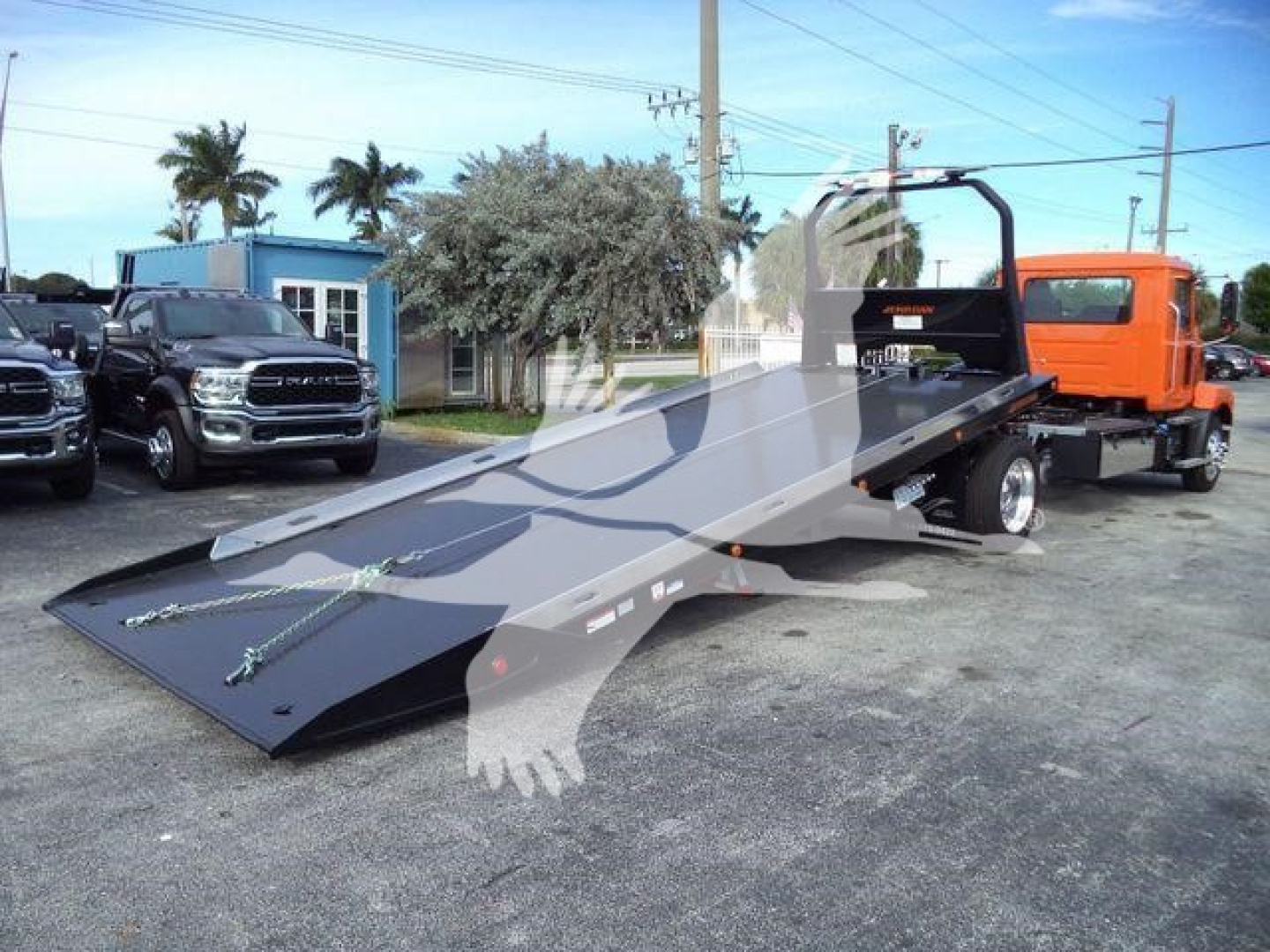 MD6 rollback tow truck with a low-profile flatbed ramp and orange cab, showing setup in a dealership lot.