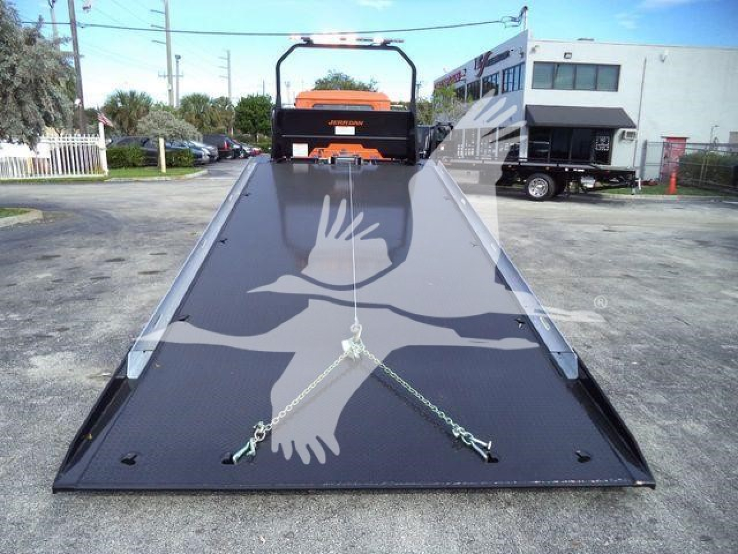 Mack MD6 rollback truck ramp with large flatbed and securing chains, in a dealership lot.