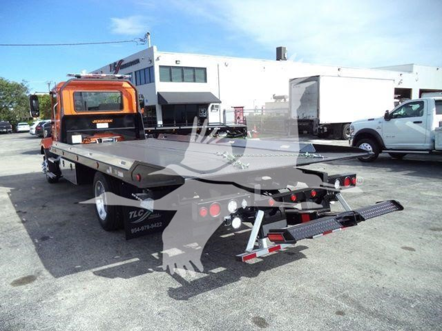 Flatbed tow truck with orange cab and rollback bed, rear view showing loading ramps and reflectors.