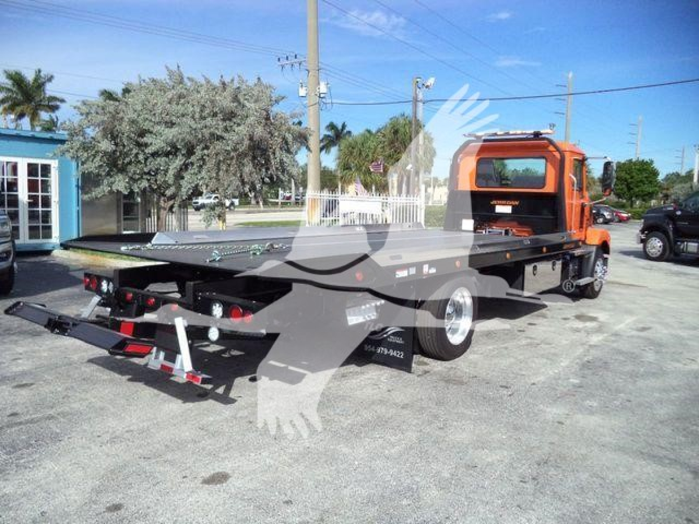 Flatbed rollback truck with orange cab and extended bed showing payload area and tail sections.
