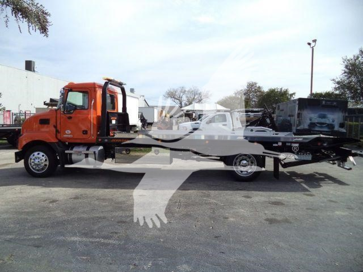MD6 tow truck side view showing orange cab and flatbed with black equipment and other vehicles in background.