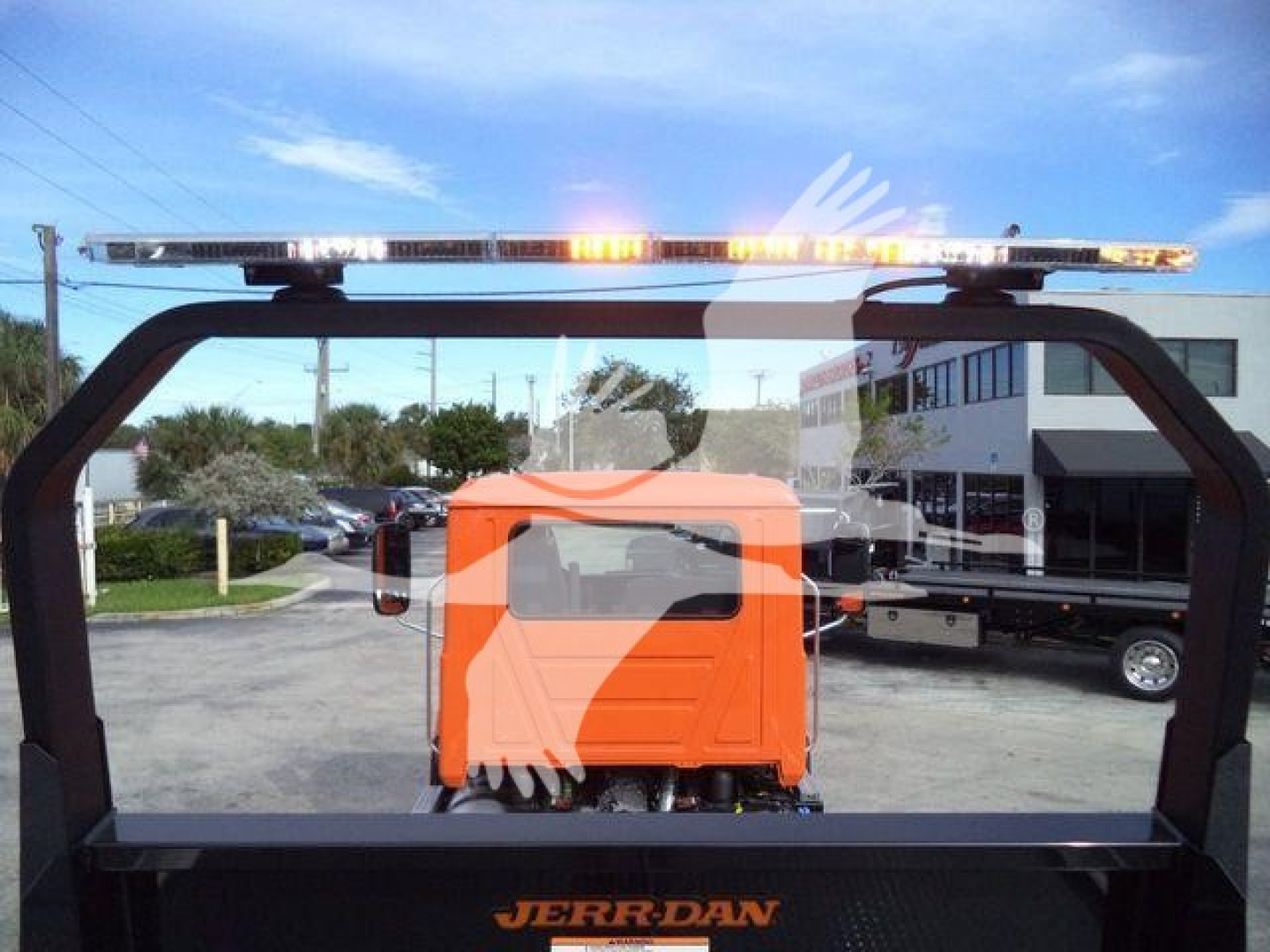 Truck view from behind showing orange Mack MD6 with Jerr-Dan rollback apparatus and amber light bar on top.