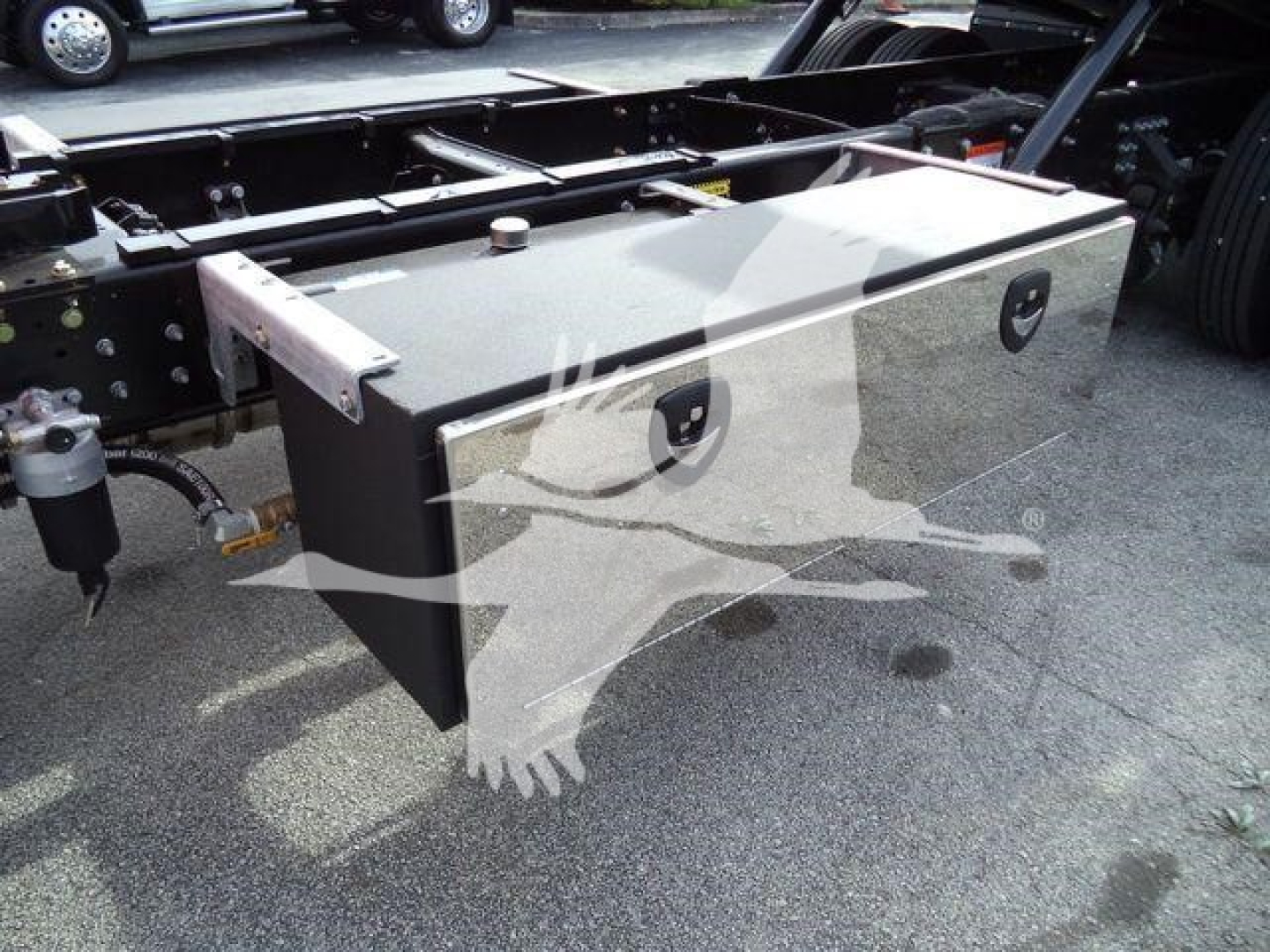 Truck chassis with large rectangular aluminum toolbox mounted between frame rails of a Mack MD6 rollback truck.