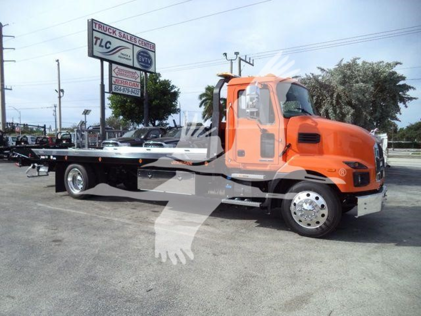 Orange Mack MD6 rollback tow truck parked at dealership lot with TLC sign in background.