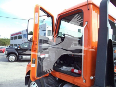 Orange Mack MD6 cab with door open, showing interior seating and controls, rollback truck in dealership yard.