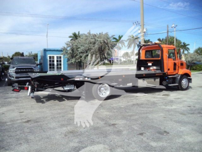MD6 rollback tow truck with orange cab and flatbed, parked on lot with another pickup in background.