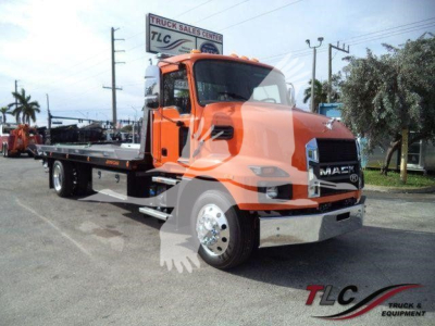 MD6 Mack truck in orange on a rollback flatbed showing Mack grille and front bumper with chrome accents; TLC Truck & Sales Center watermark in lower right.