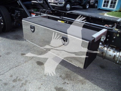 Large aluminum toolbox mounted under Mack MD6 truck frame with two latches, reflective surface, and mounting brackets visible.