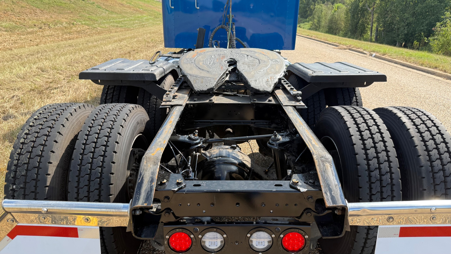 Kenworth W900 chassis and rear wheels view showing dual rear axles and fifth wheel with components visible.
