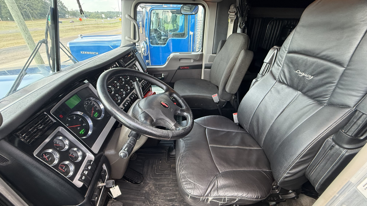 Kenworth W900 truck interior showing steering wheel, dashboard gauges, and black leather seats in a sleeper cab.
