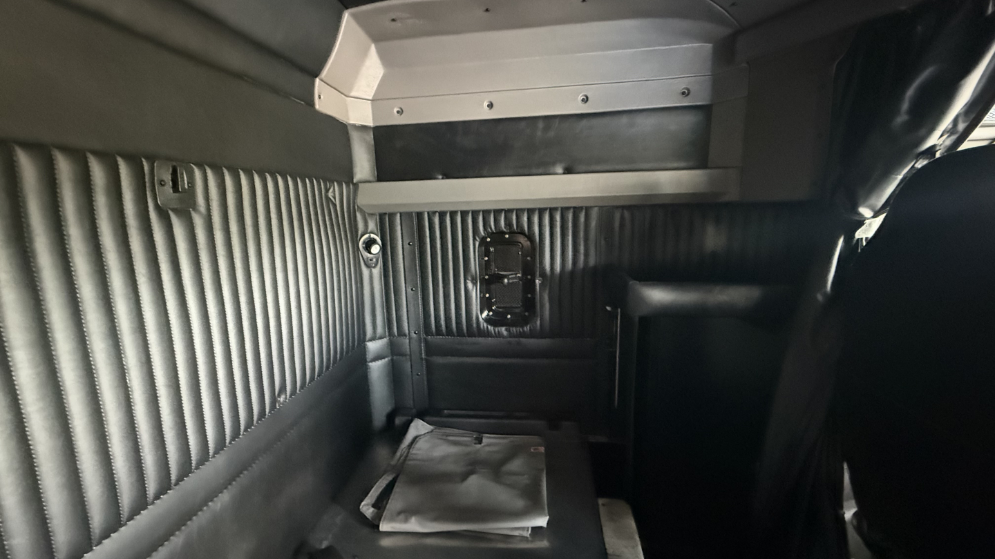 Kenworth W900 sleeper cab interior showing ribbed metal side panels and a small rectangular rear window opening.