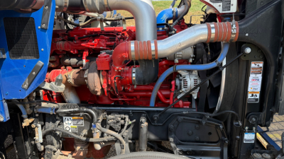 Kenworth W900 engine bay with red engine, silver turbo pipes, blue accents, and various hoses; visible components include hoses, belts, and an alternator.