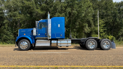 Kenworth W900 tractor in profile view showing blue cab and sleeper with chrome steps and dual rear axles.
