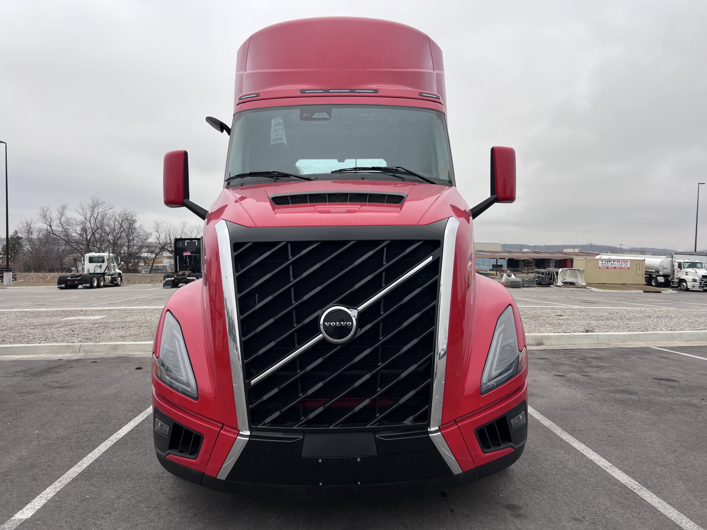 Front view of a red 2025 Volvo VNL64T300 truck showing the grille with Volvo emblem, headlights, and side mirrors.