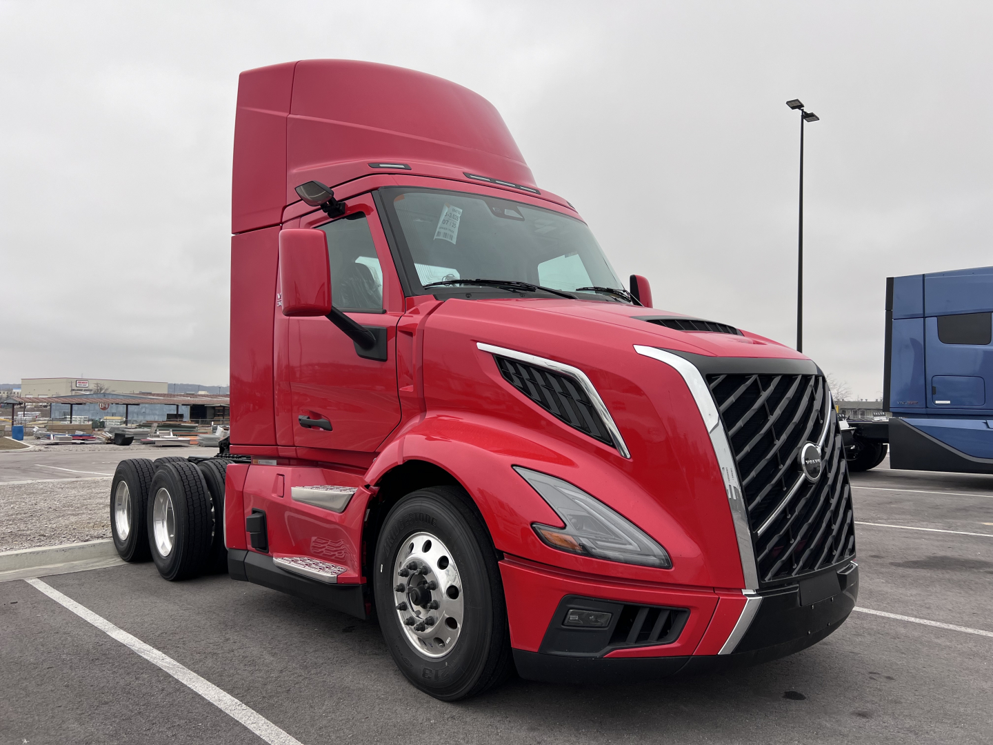 Volvo VNL64T300 tractor in red, front-left view, showing cab and grille with chrome accents, triple-axle rear, side mirrors, and Volvo emblem.