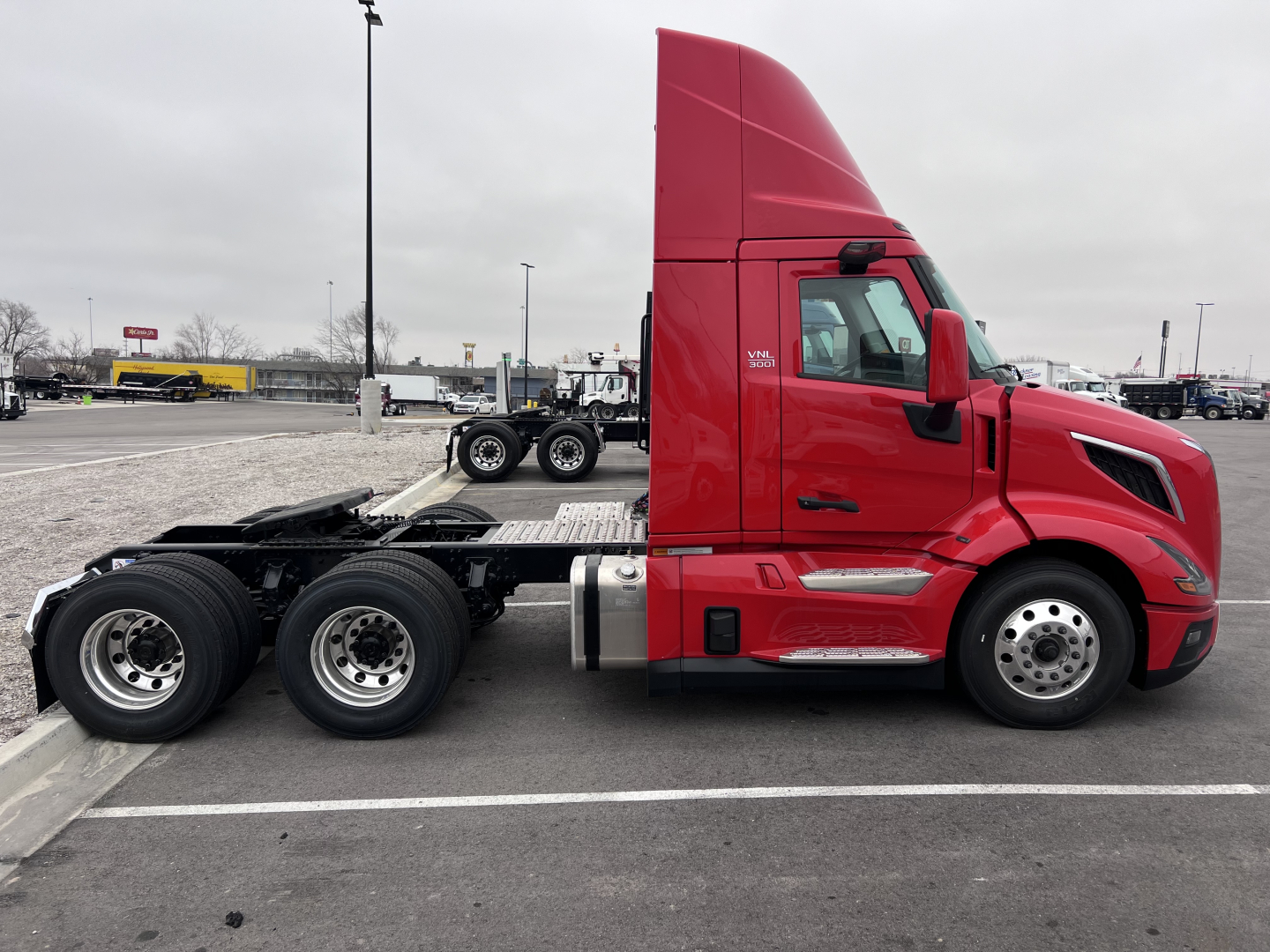 Volvo VNL64T300 truck tractor side profile showing bright red cab and chassis with dual rear axles and empty fifth wheel mount.