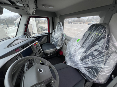 Volvo VNL64T300 truck cab interior showing driver seat and passenger seat covered in plastic, steering wheel, dashboard, and center console.
